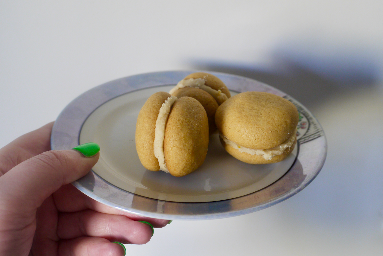 A hand with green nailpolish holding a white and blue plate with three cookies on it against a white background
