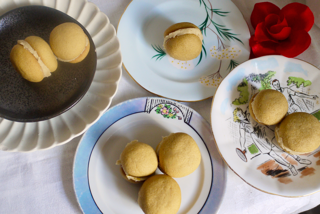 Cookies on a selection of small plates with a red fabric rose and a white tablecloth