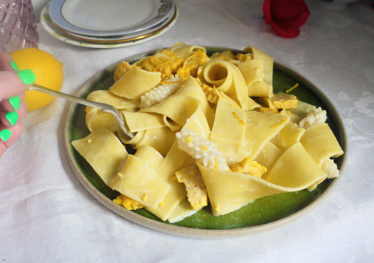 hand with green nails twirling pappardelle on a green plate