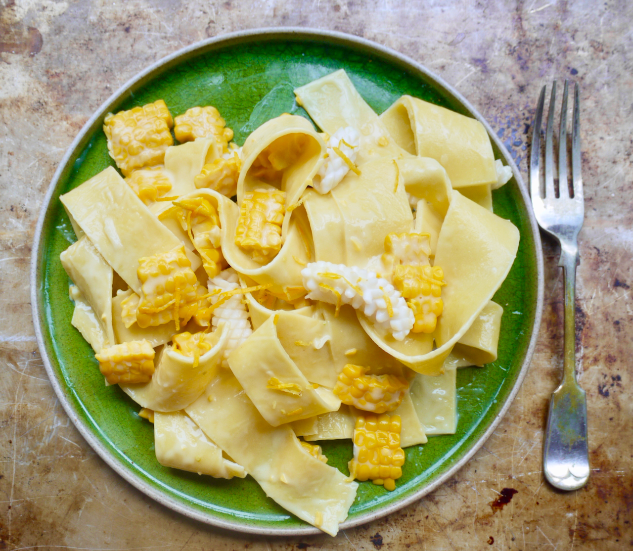 pappardelle, corn and squid on a green plate with a fork