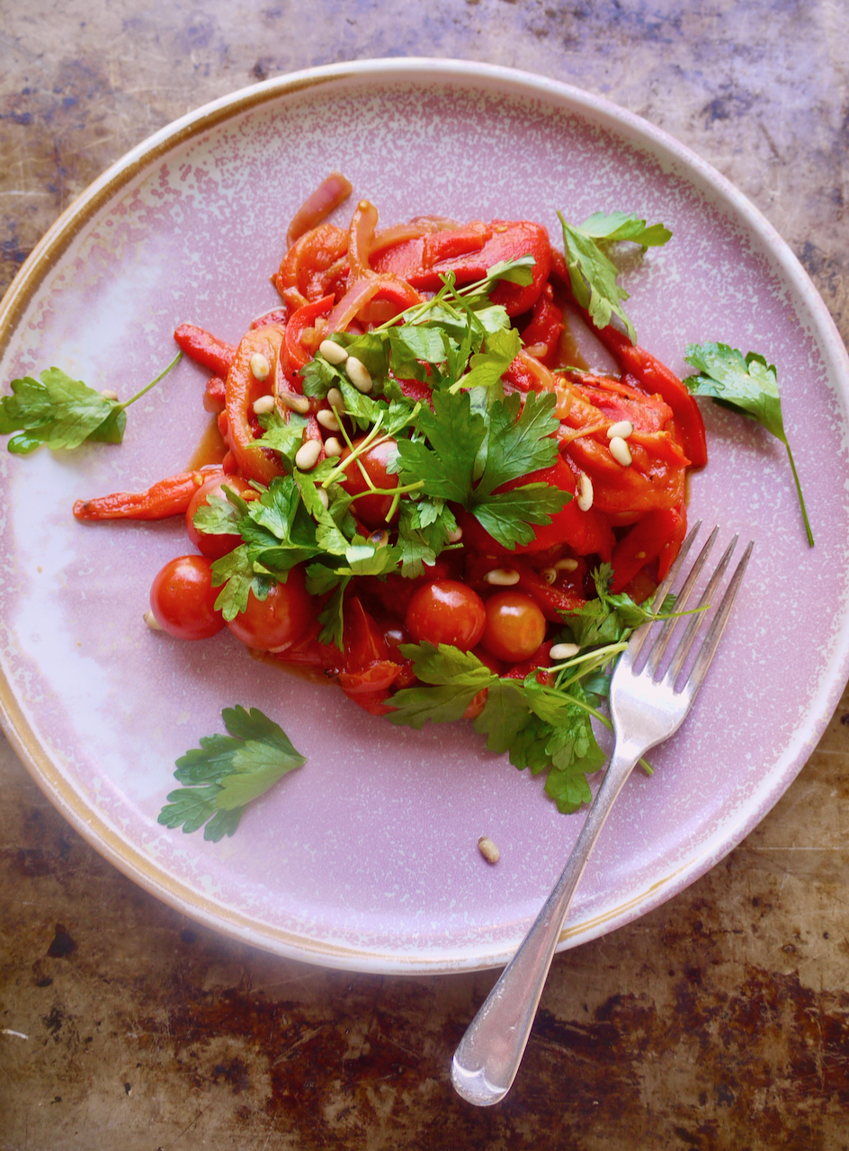 A pink plate of piperate with a fork resting on it, on a metal baking sheet