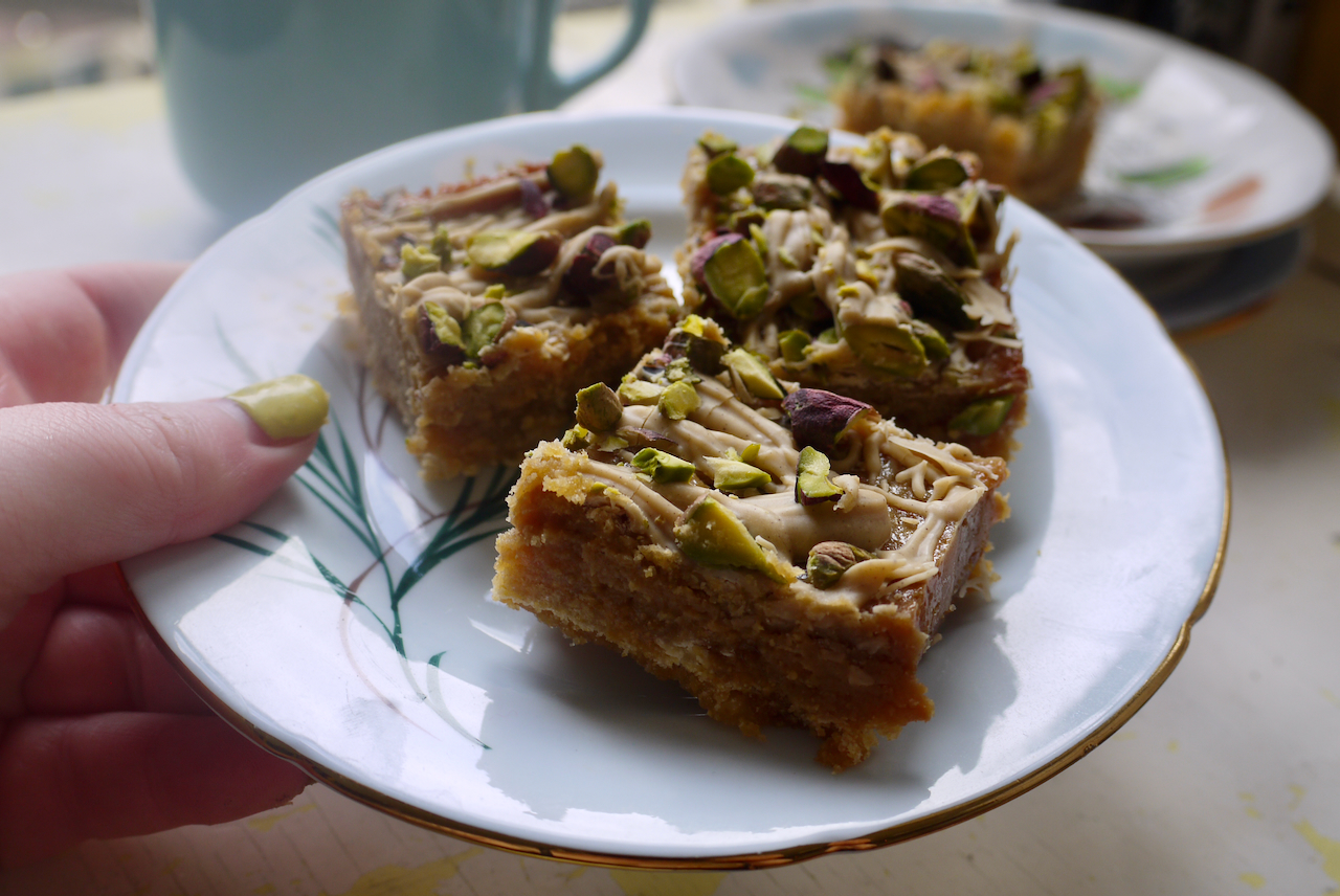 A hand with yellow green nails holding a blue plate of caramel slice