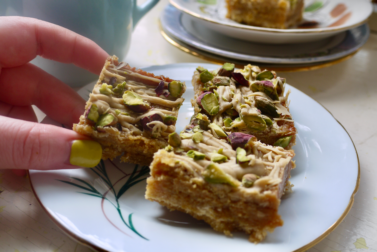 a hand with yellow-green nails picking up a piece of caramel slice