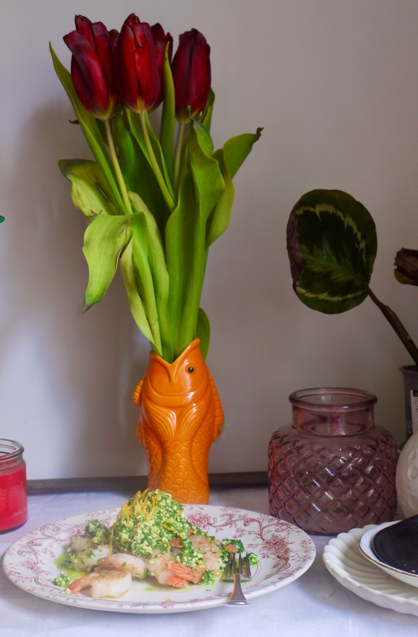 A plate of prawns and rocket with an orange vase of tulips in the background