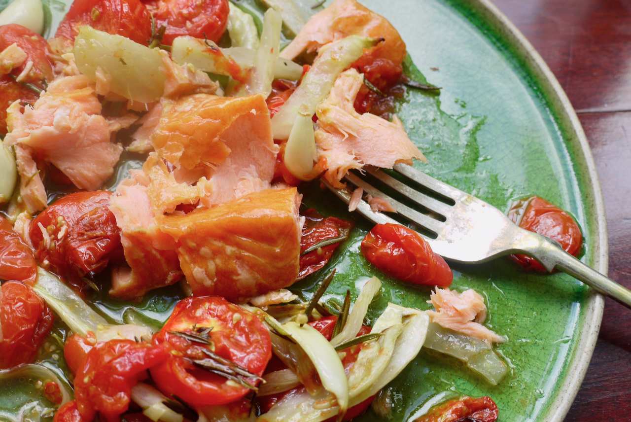 A plate of roasted cherry tomatoes, forked-apart salmon, and fennel