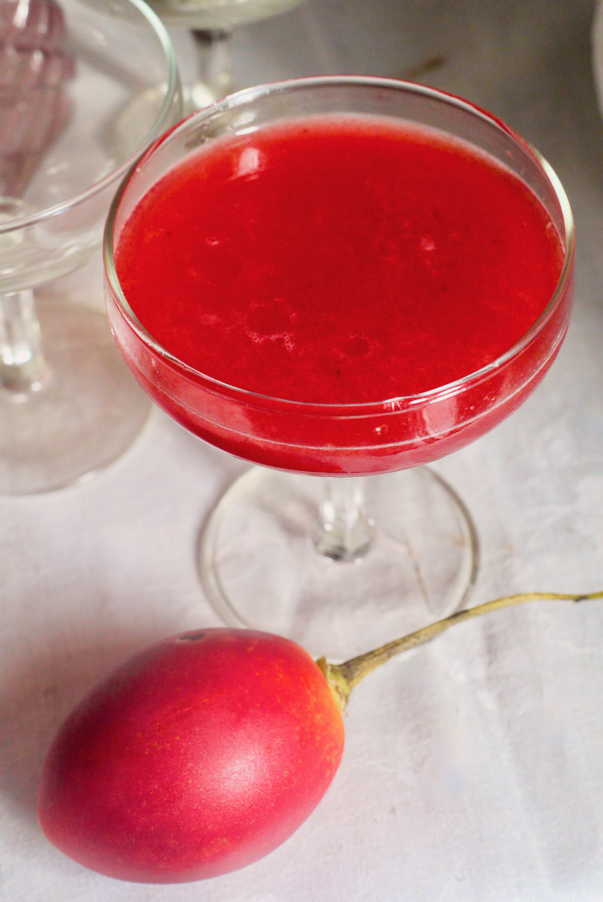 A tamarillo cocktail on a white tablecloth with a tamarillo in front of it