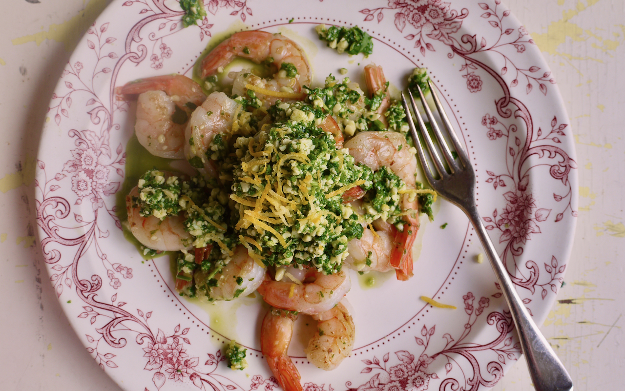 A white plate with pink floral border, with prawns and rocket piled up on it along with a fork