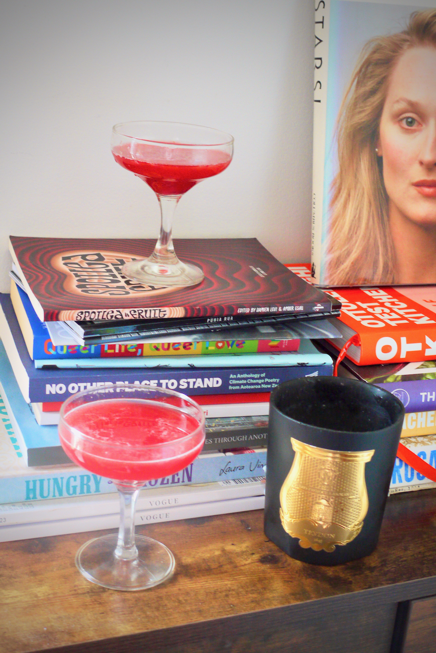 Two tamarillo cocktails, one on a stack of books and one in front on a ledge, with a book in the background with Meryl Streep's face on the cover