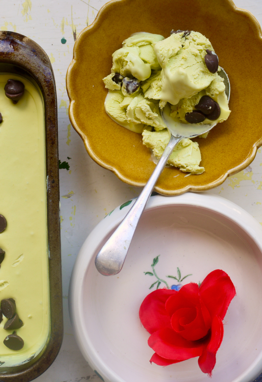 a brown bowl of mint choc chip ice cream with a spoon next to a red fabric flower in a bowl