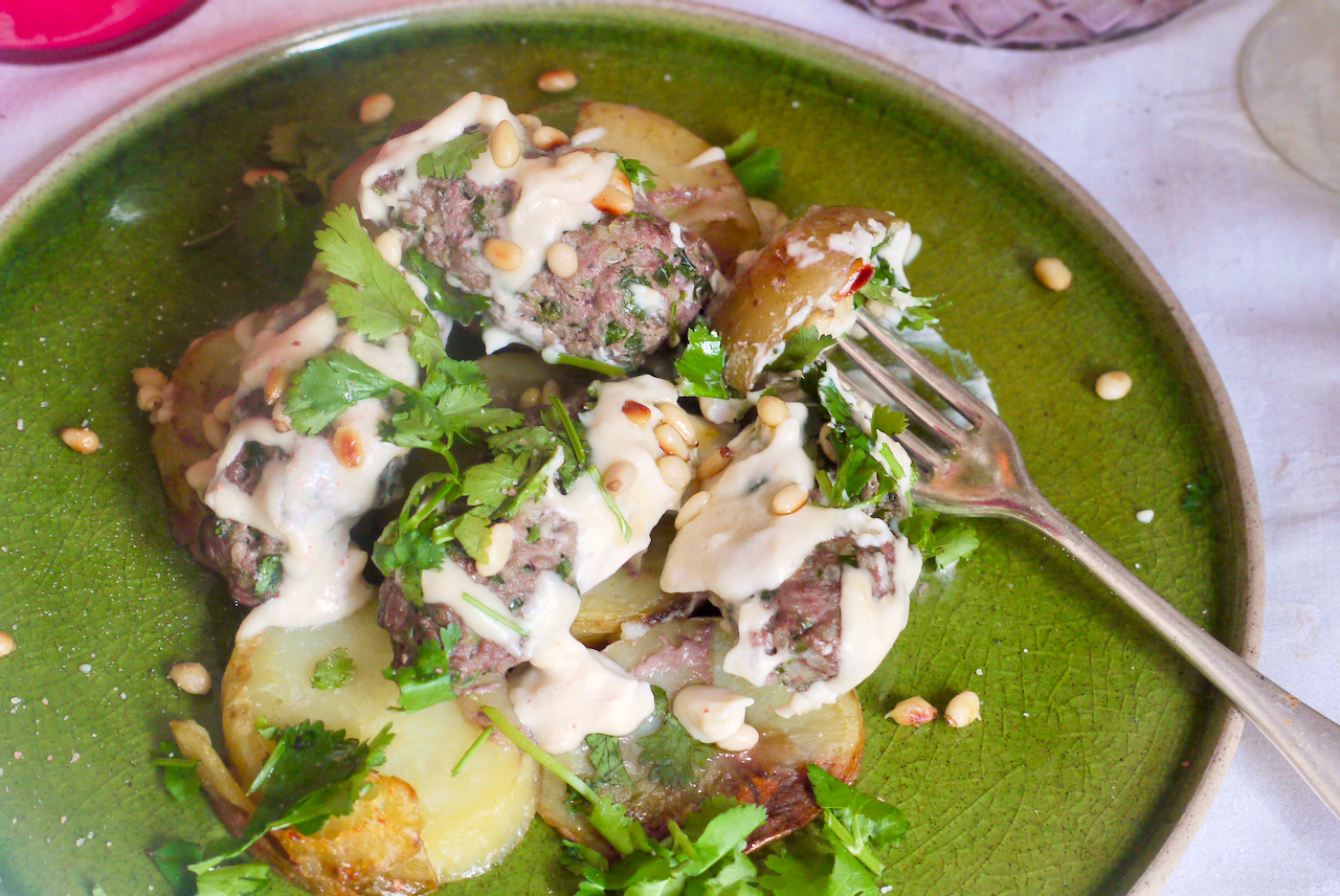 A forkful of potato on a green plate with lamb kefte on a white tablecloth