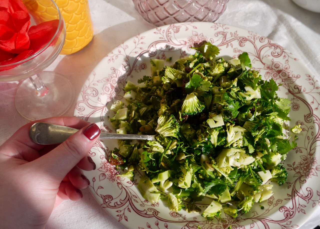 A hand with red fingernails using a fork to pick up broccoli salad