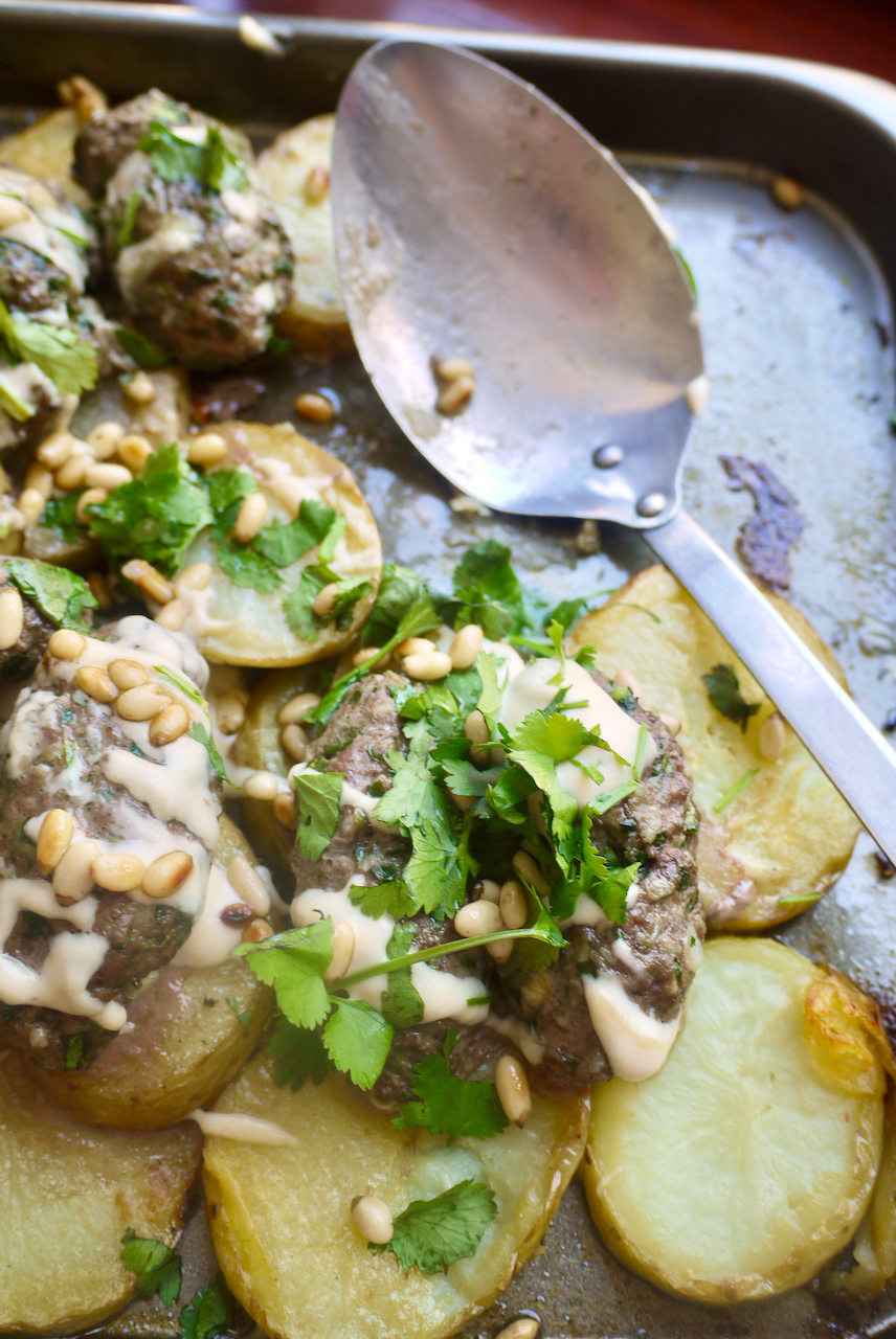 A roasting tray of potatoes and lamb kefte with a large serving spoon