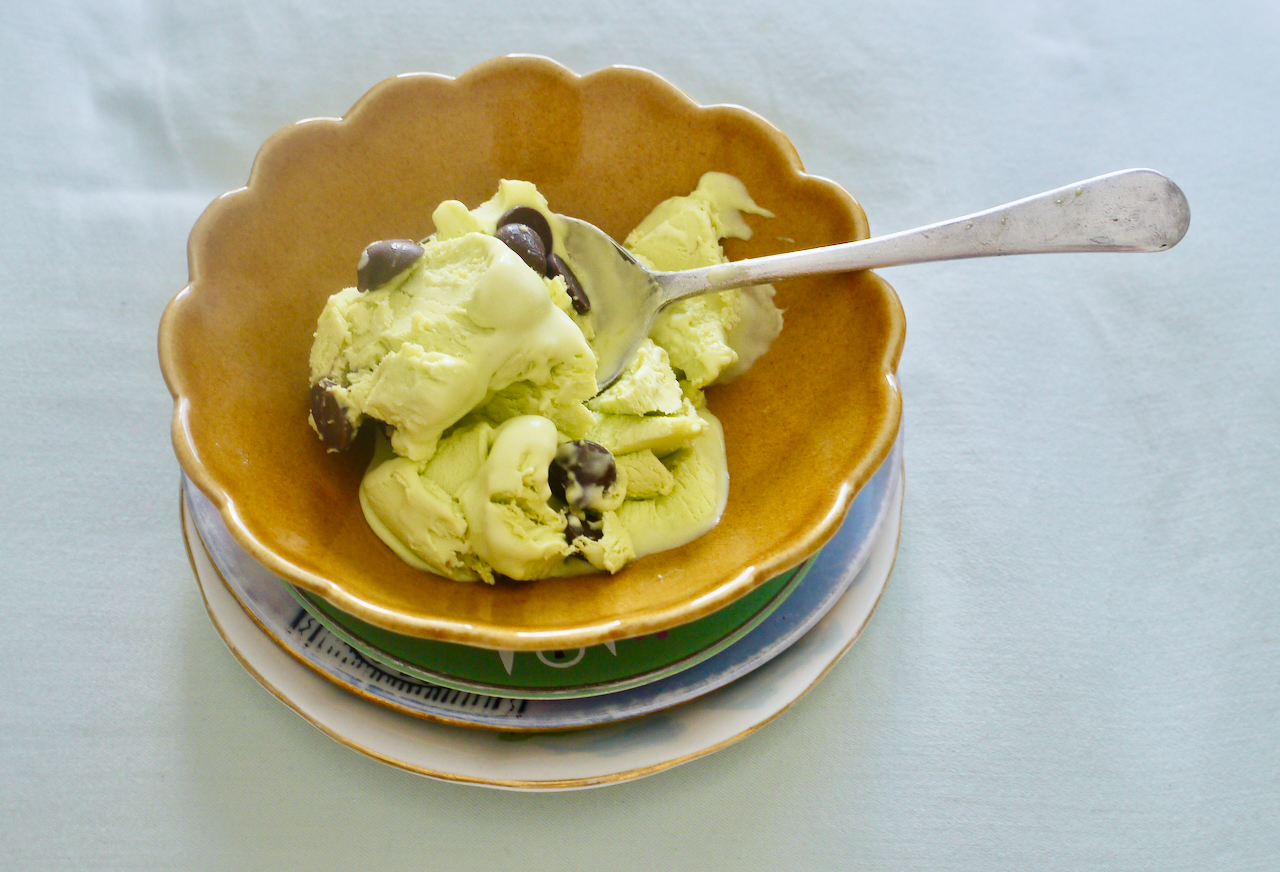 mint choc chip ice cream in a brown bowl on a stack of small plates on a sage green background