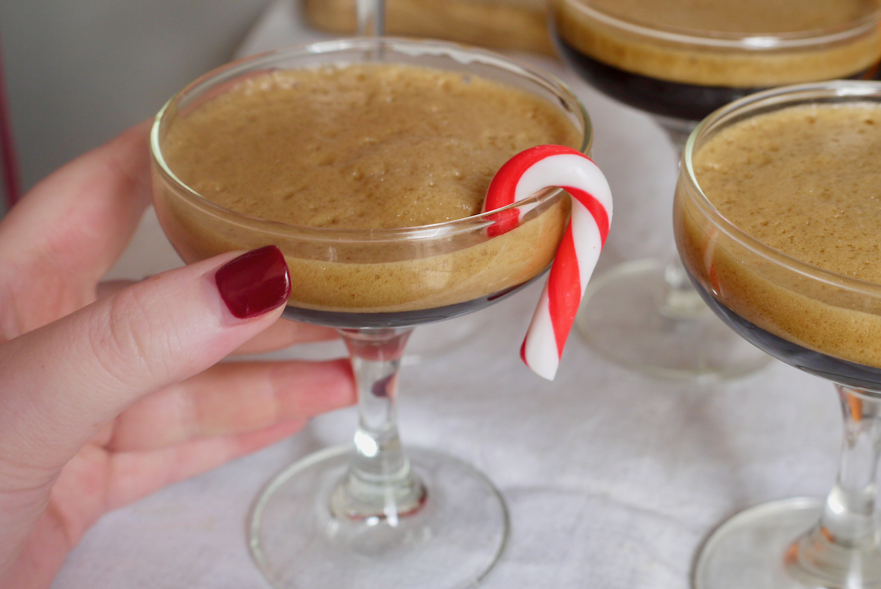 a hand with red nails holding an espresso martini with a candy cane