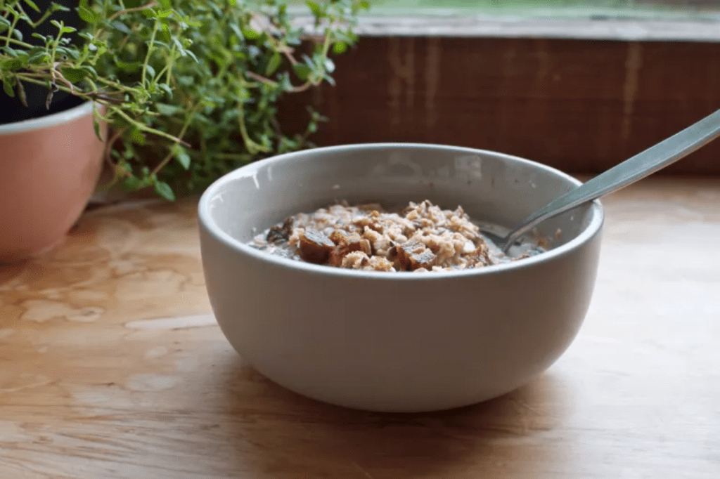 A grey bowl of granola with a spoon in it in front of a herb plant. This image links through to a web page with the recipe. 