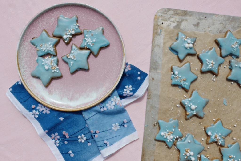 Blue-iced star shaped cookies on a pink plate and tray. This image links through to a web page with the recipe.