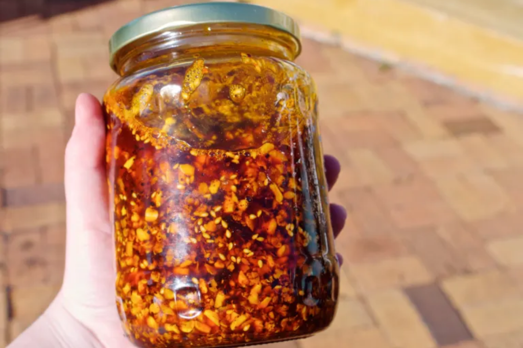 A hand holding a jar of chilli crisp. This image links through to a web page with the recipe.
