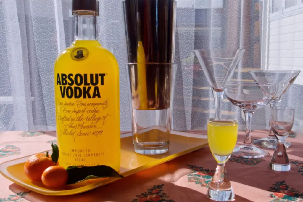 A bottle of mandarin liqueur with two mandarins in front of it, with several glasses and a cocktail shaker in the background. This image links through to a web page with this recipe.