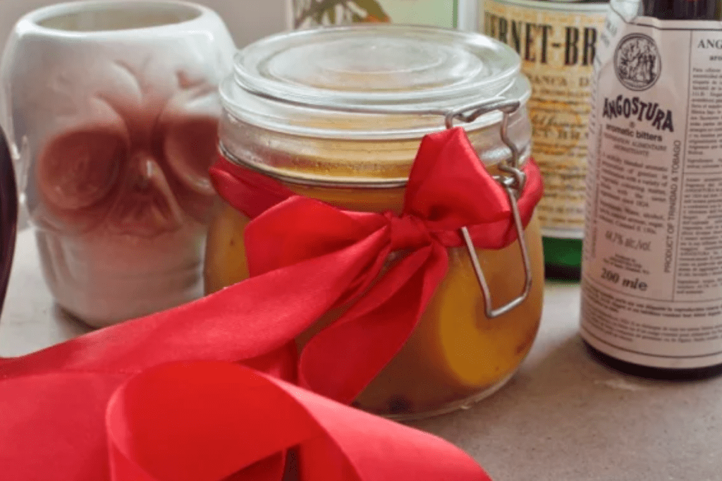 A jar of peaches with a large red bow on it, and a skull mug behind it. This image links through to a web page with the recipe.