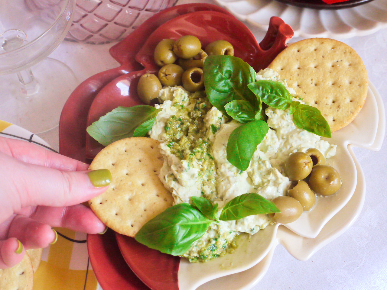 A hand with green nails scooping dip with a cracker