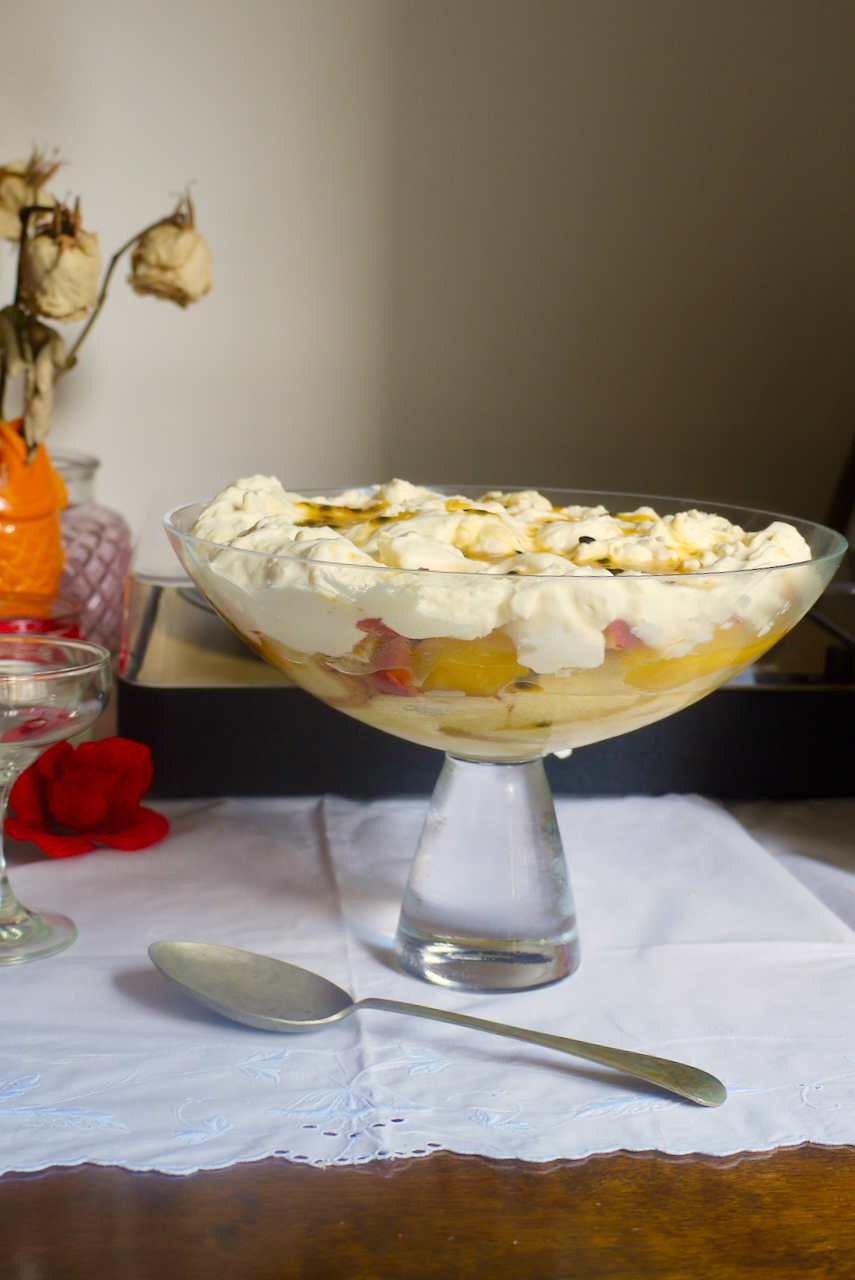 a bowl of trifle with an orange vase of dried roses