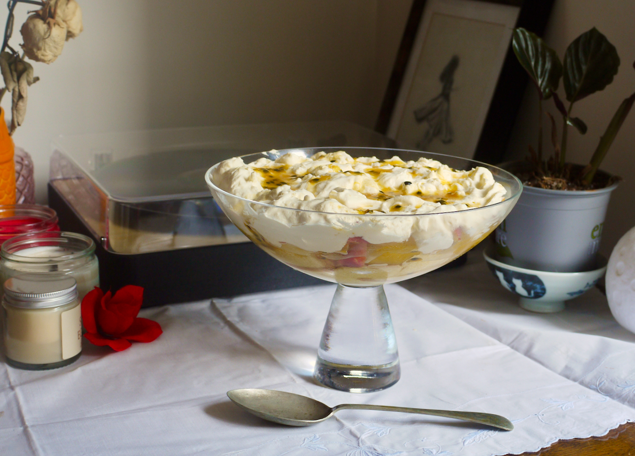 a spoon on a white tablecloth in front of a bowl of trifle