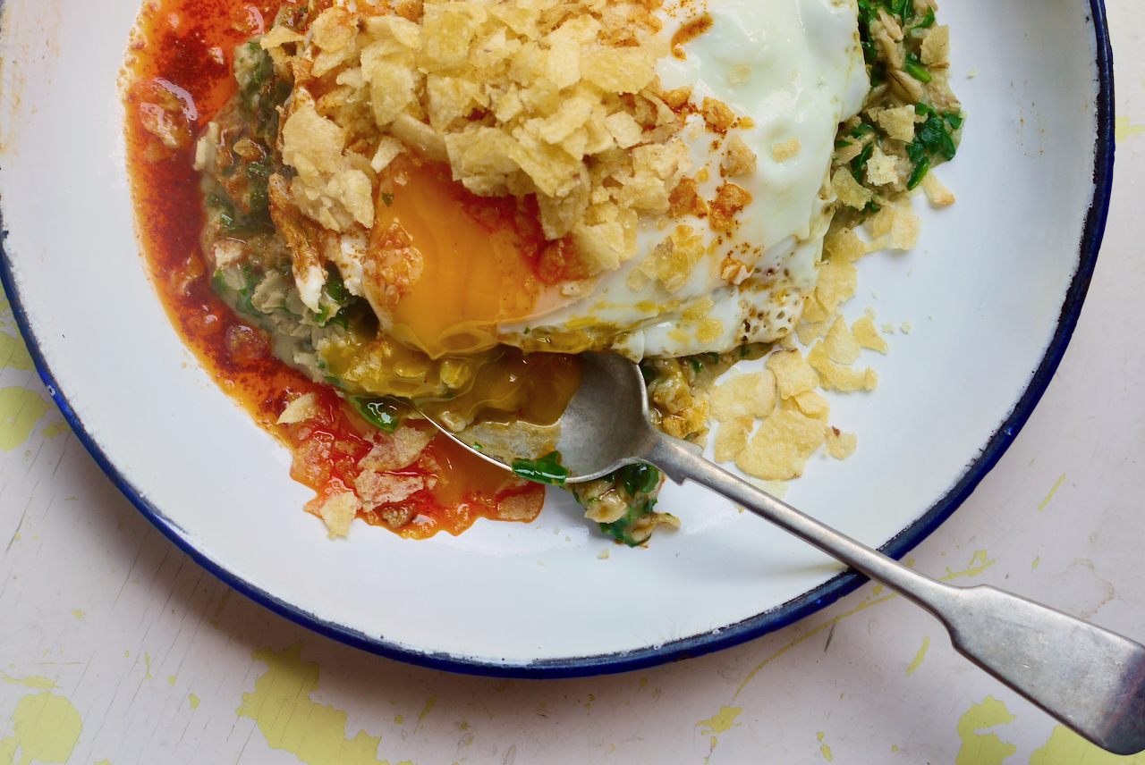 the runny yolk of a fried egg with crushed chips on top, running into a spoon