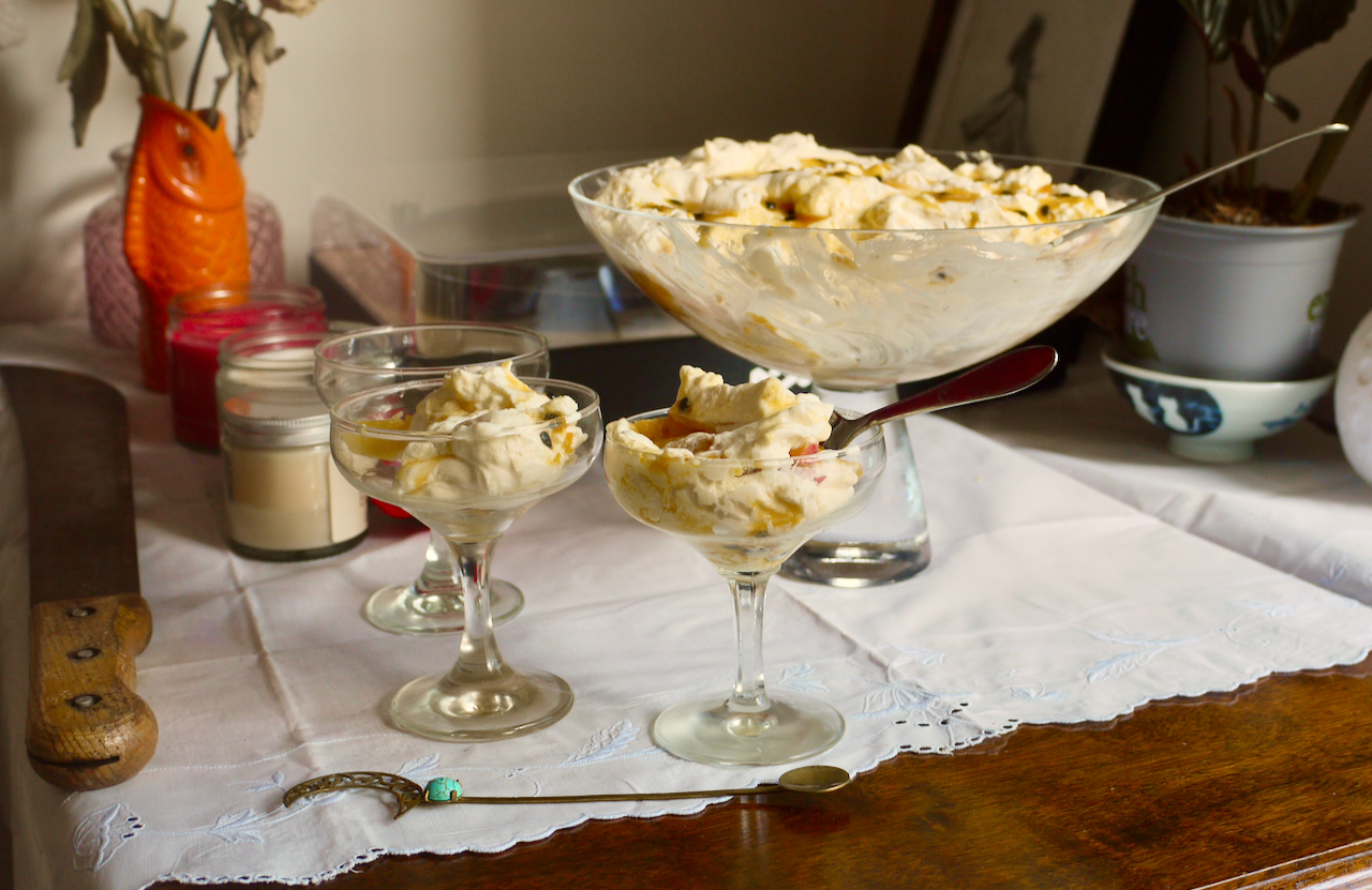 two coupe glasses of trifle in front of a large bowl of trifle