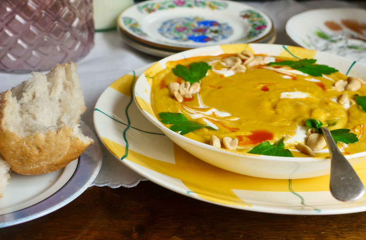 a bowl of butternut soup with a piece of bread next to it