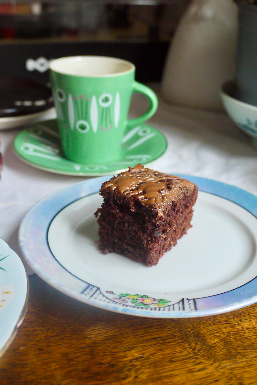 A slice of cake on a blue and white plate with a green coffee cup behind it