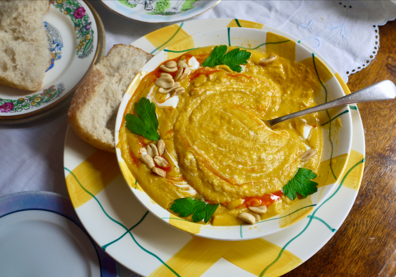 a spoon in a bowl of butternut soup with a piece of bread resting on the plate below