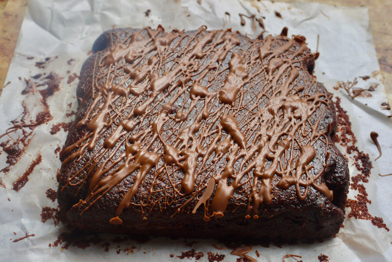 A square chocolate cake drizzled in melted chocolate