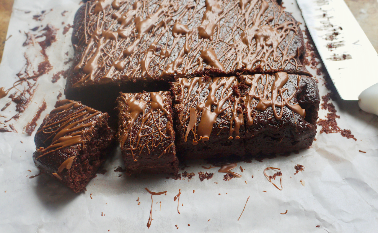 A square chocolate cake with slices cut out of it and the knife next to it