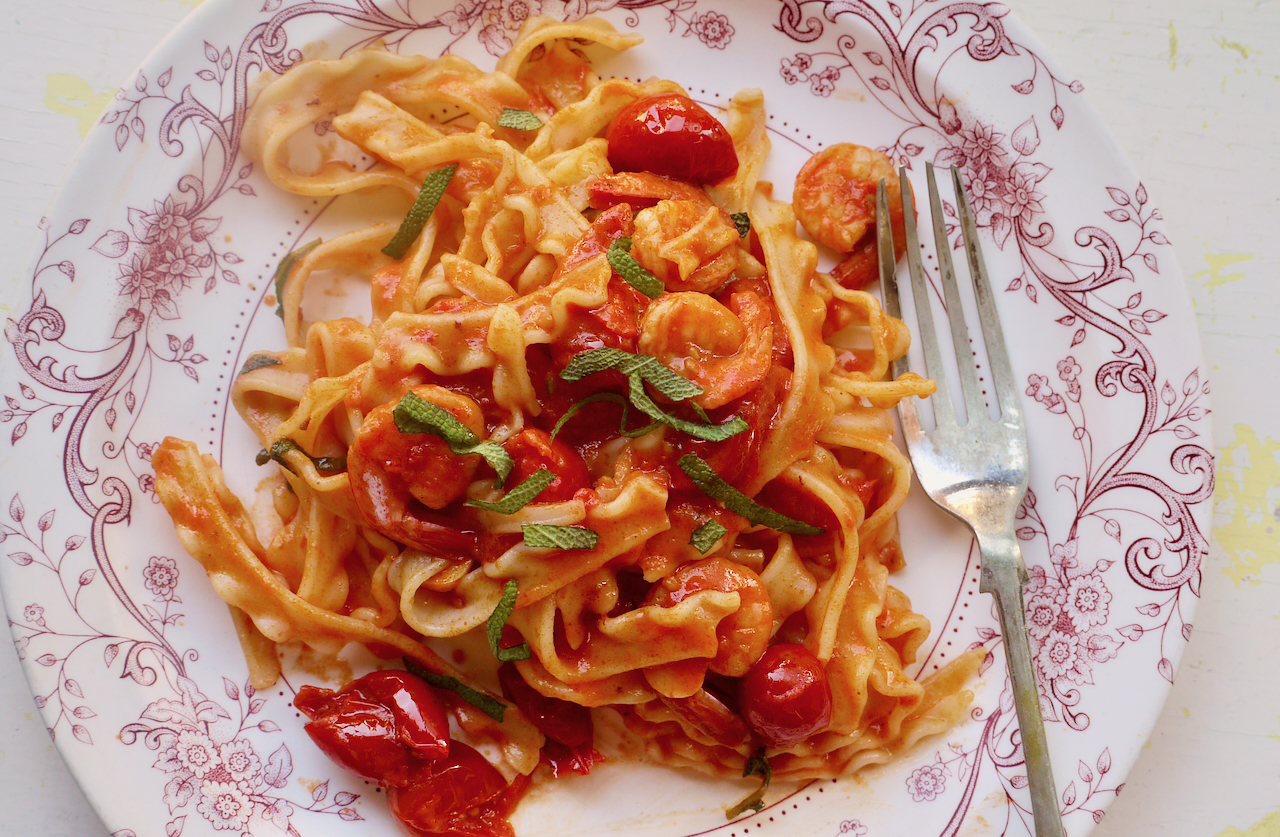 A white plate with a pink patterned border, full of tomato pasta with a fork resting on it