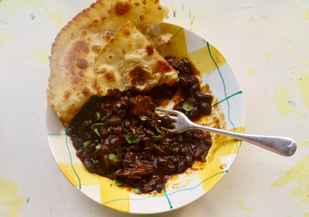 A yellow and white bowl of chilli with flatbread and a fork