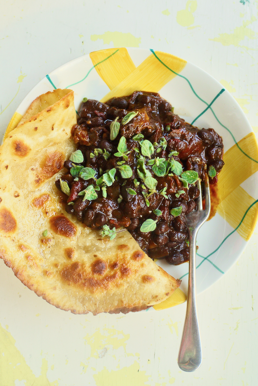 A yellow checked bowl of chilli and flatbread on a white background with a fork resting on it