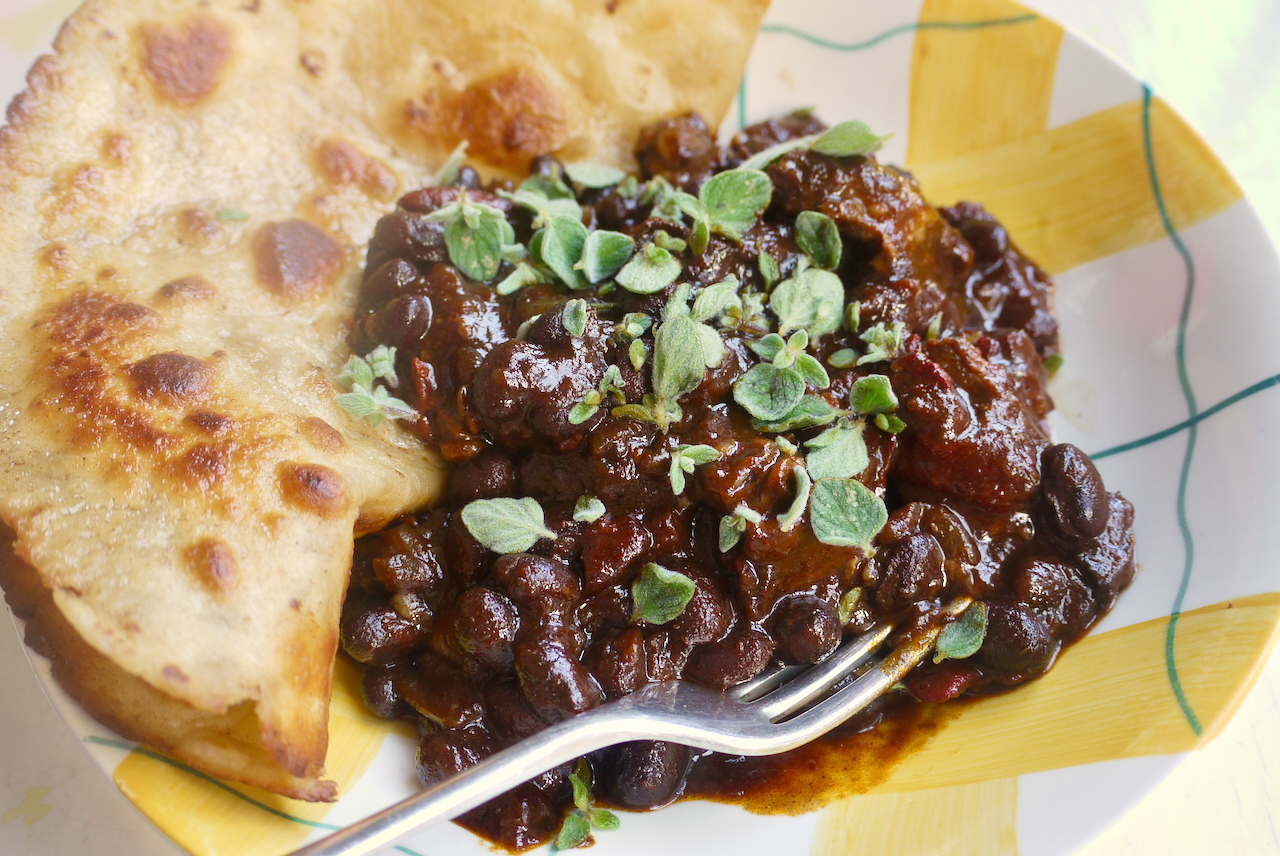 Close up of a fork resting in a bowl of chilli with oregano leaves