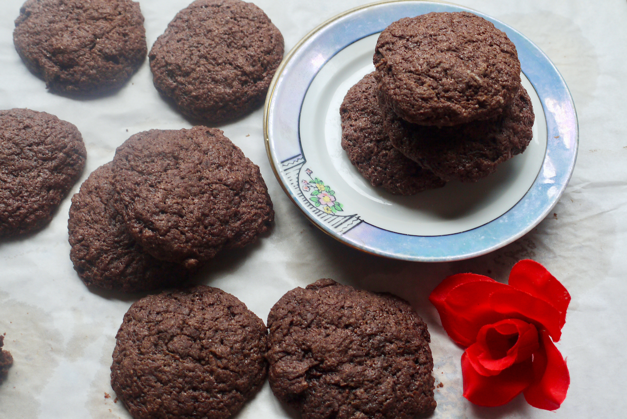 Cookies on a tray with several stacked on a blue and white plate, with a red fabric rose next to them