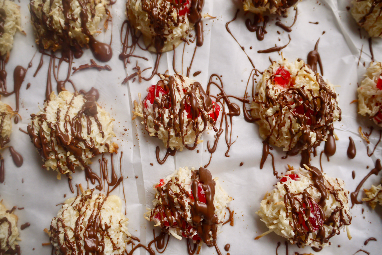 A baking tray of plain and cherry macaroons, drizzled with chocolate