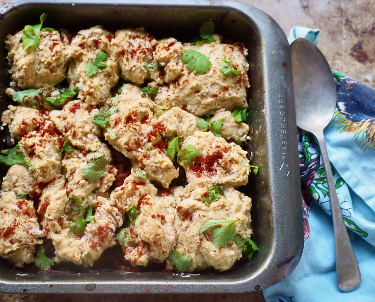 A dish of black bean cobbler with a spoon and a blue teatowel