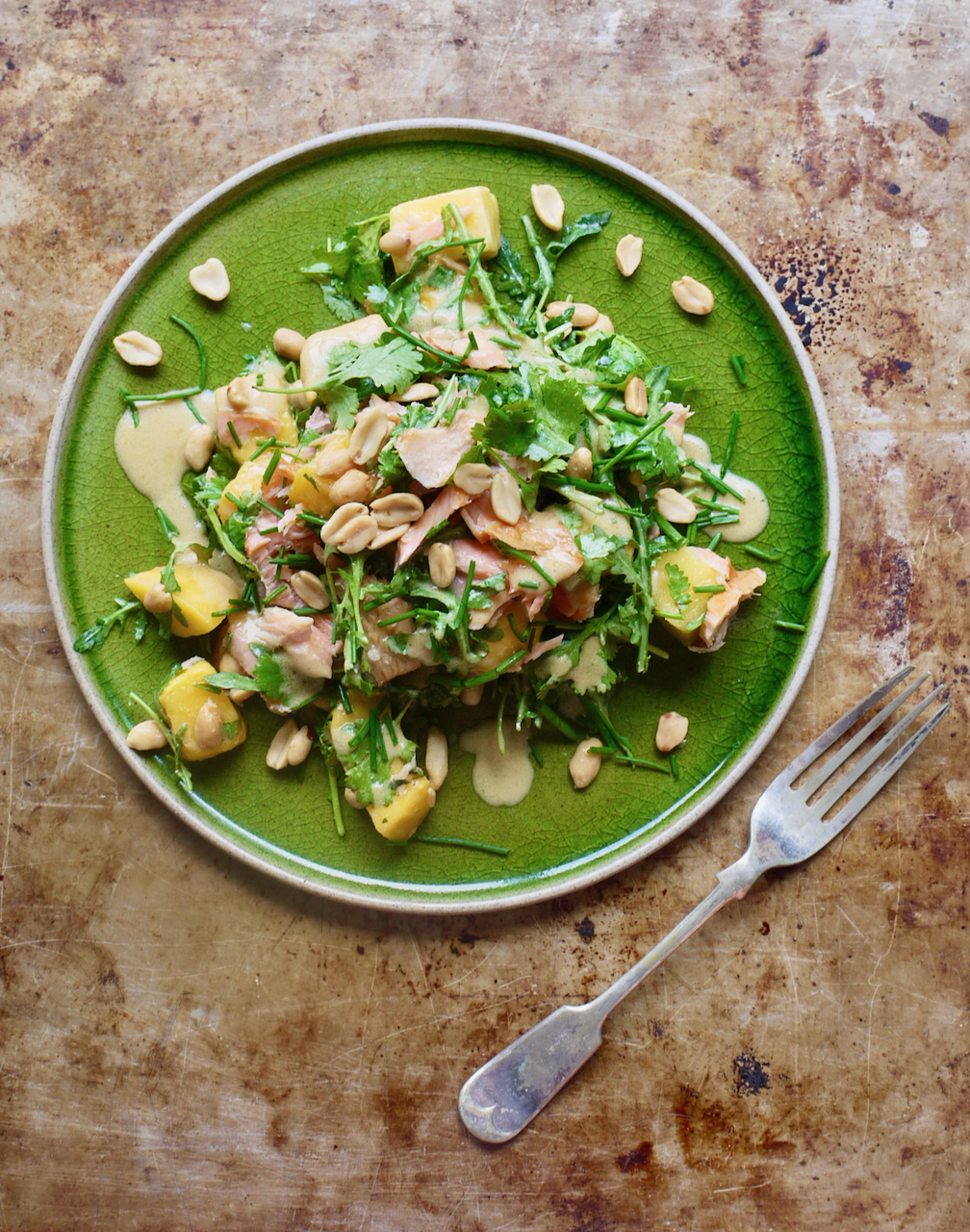 Salmon mango salad on a green plate, on a baking tray with a fork below it
