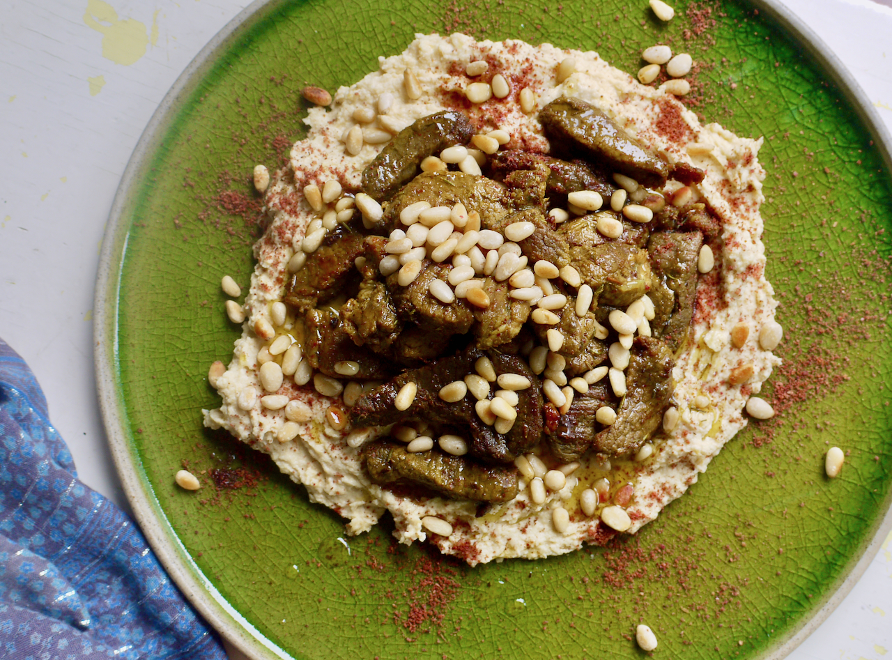 a green plate of hummus and lamb on a white background with blue fabric