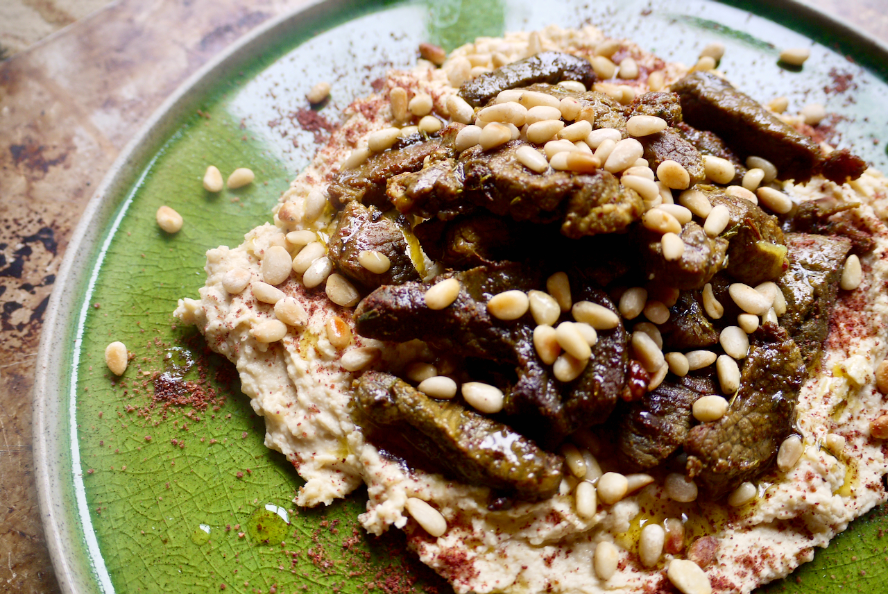 A green plate of hummus and lamb with pine nuts