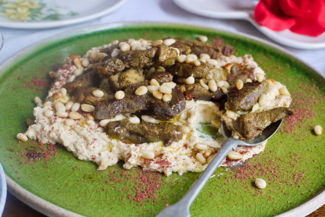 A spoonful of hummus and lamb on a green plate