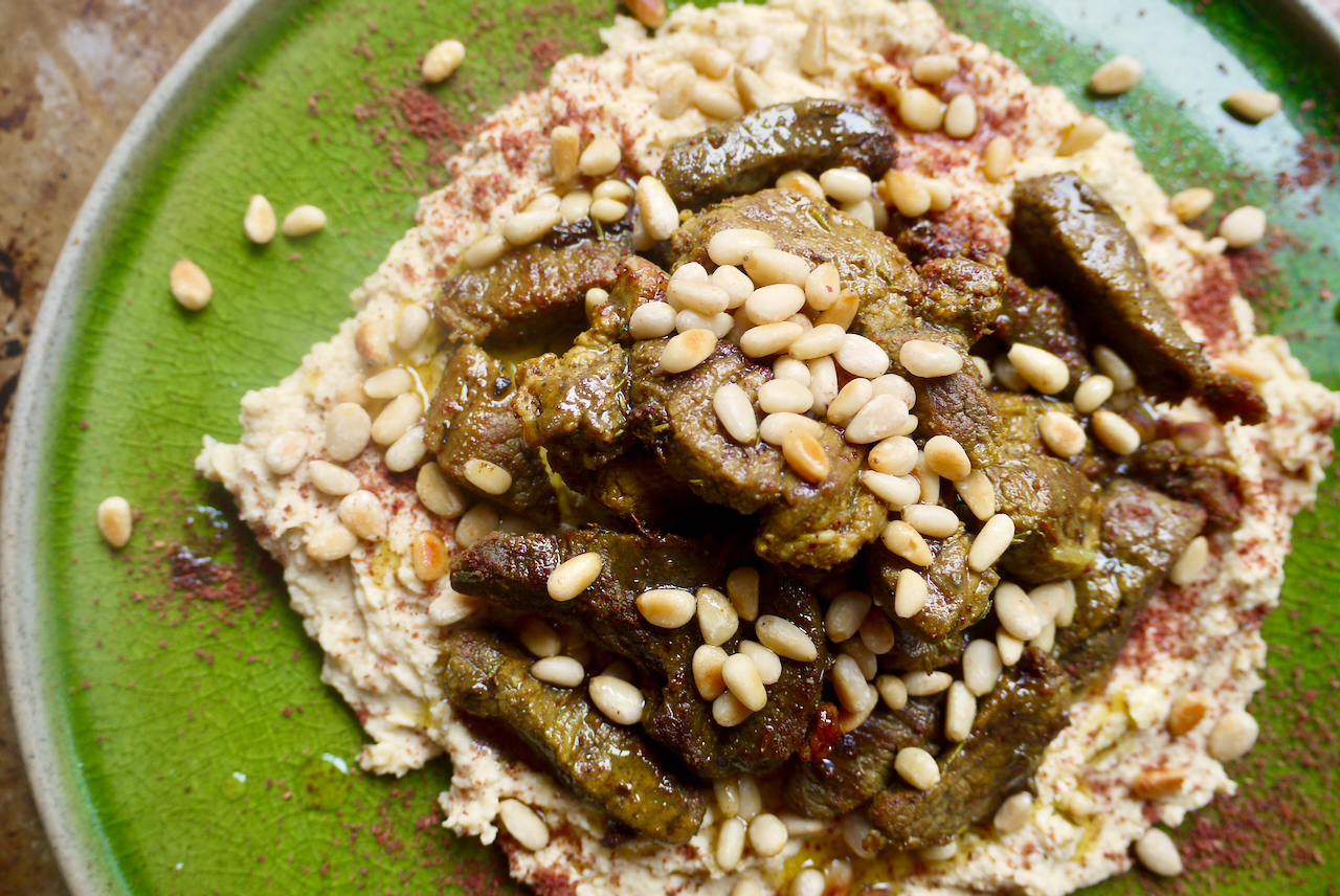 Hummus and lamb with pine nuts on a green plate