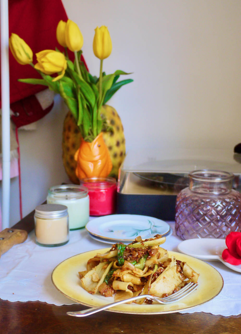A plate of noodles on a table with a vsase of yellow flowers