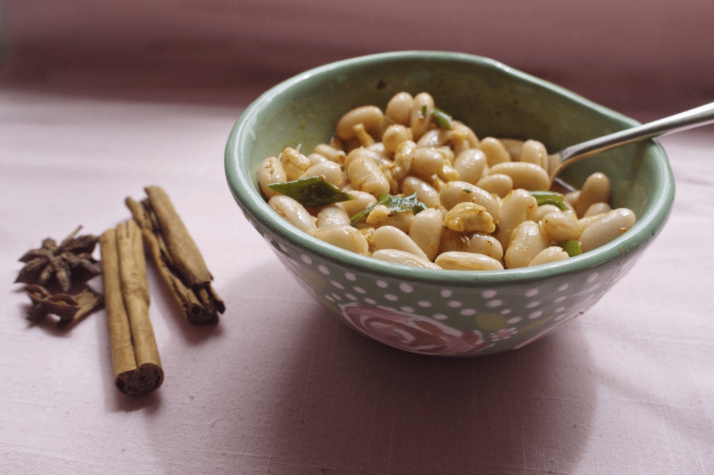 Chilli oil beans in a green bowl on a pink background with cinnamon sticks and star anise beside it. This image links to a web page with this recipe.