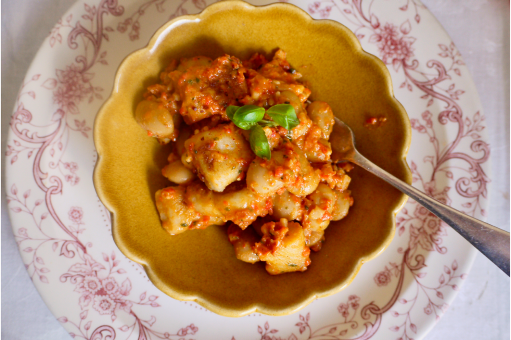 A brown scalloped bowl of gnocchi resting on a pink and white plate. This image links to a web page with this recipe.