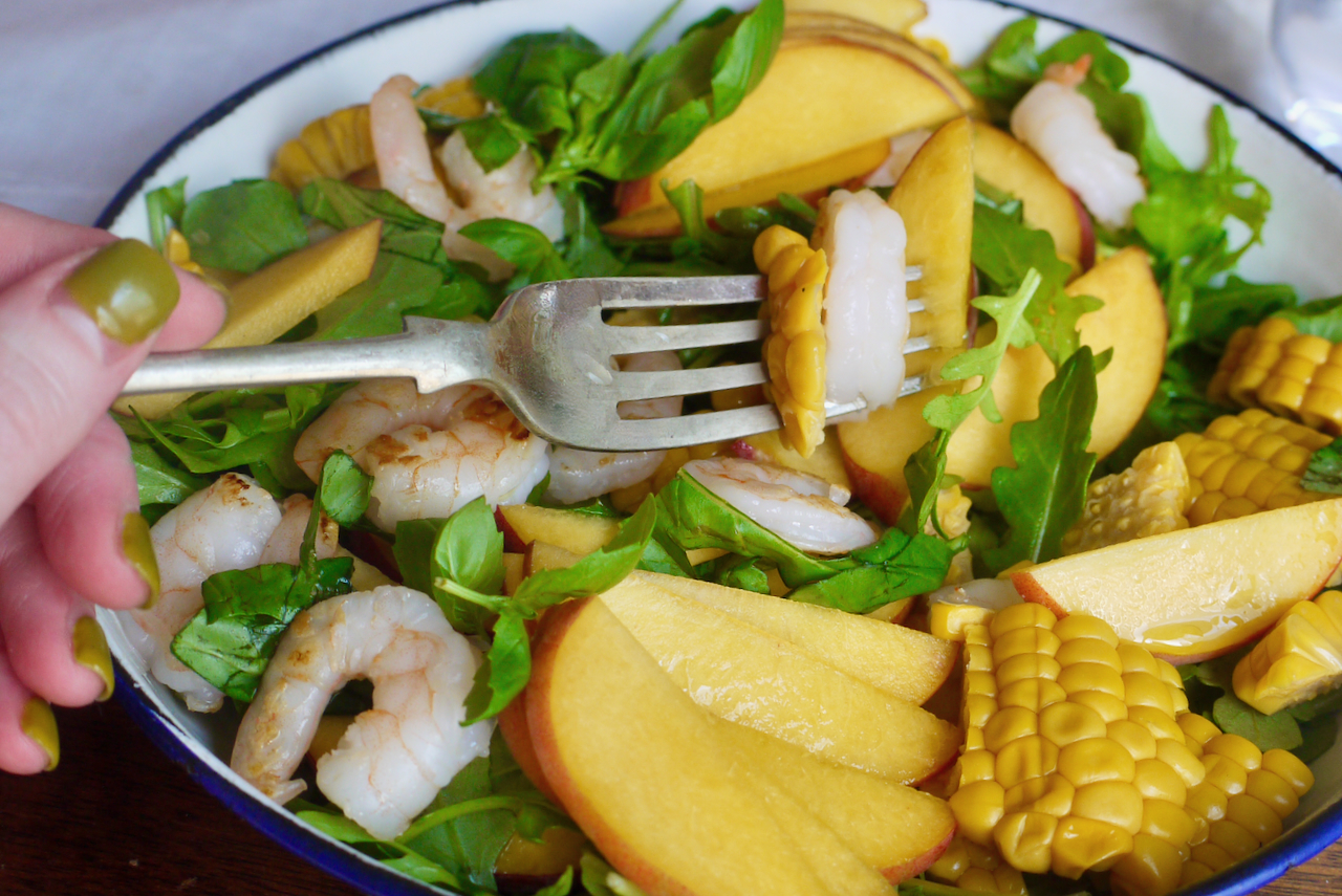 A hand with green painted nails holding a forkful of corn prawn and peach salad