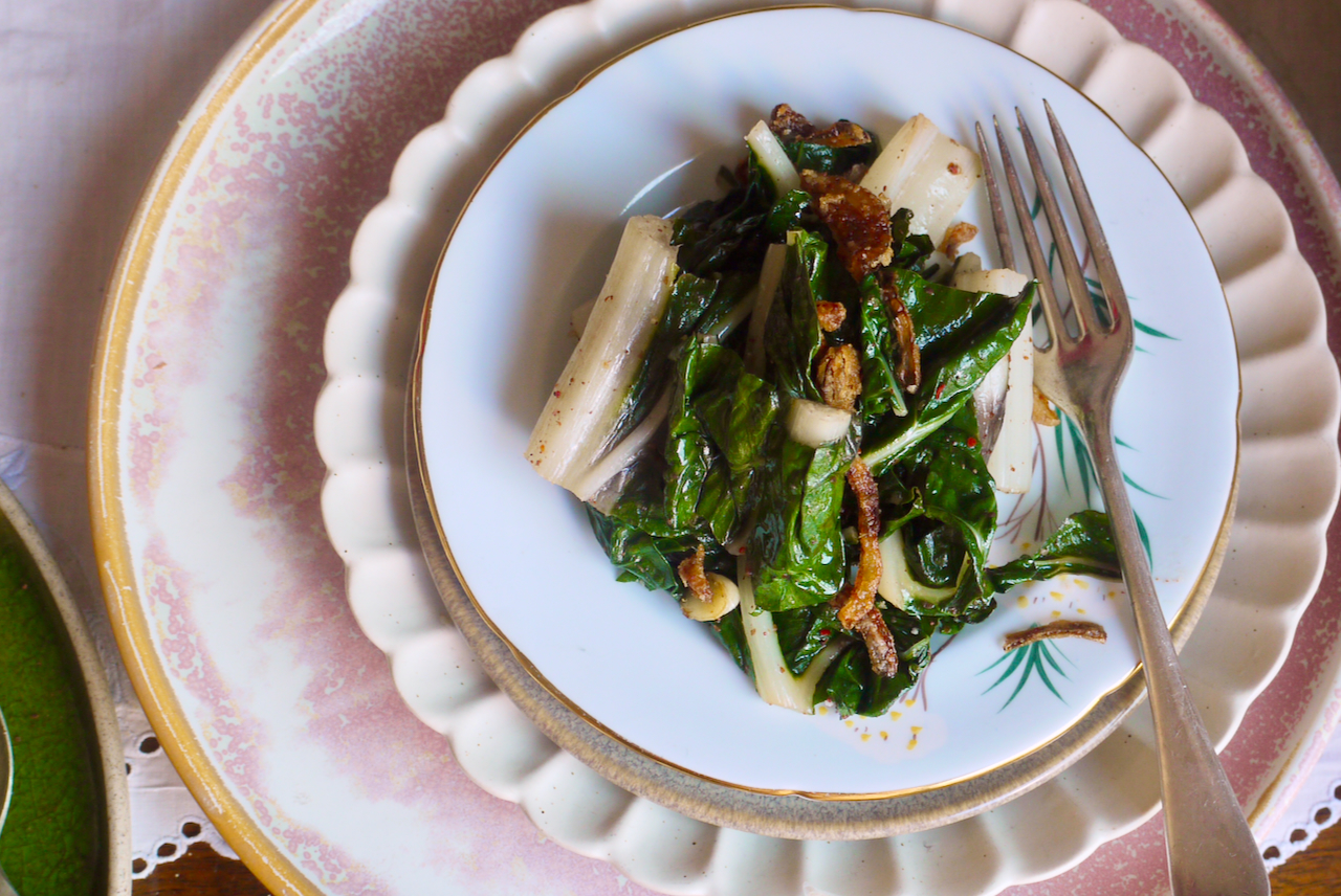 Braised silverbeet and fried onions on a light blue plate, sitting atop a white fluted plate
